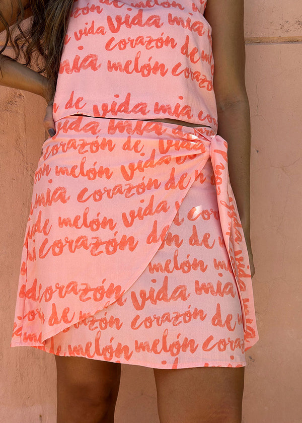 A person wearing a short pink skirt with a text pattern, waist tie, and a visible zipper at the back.